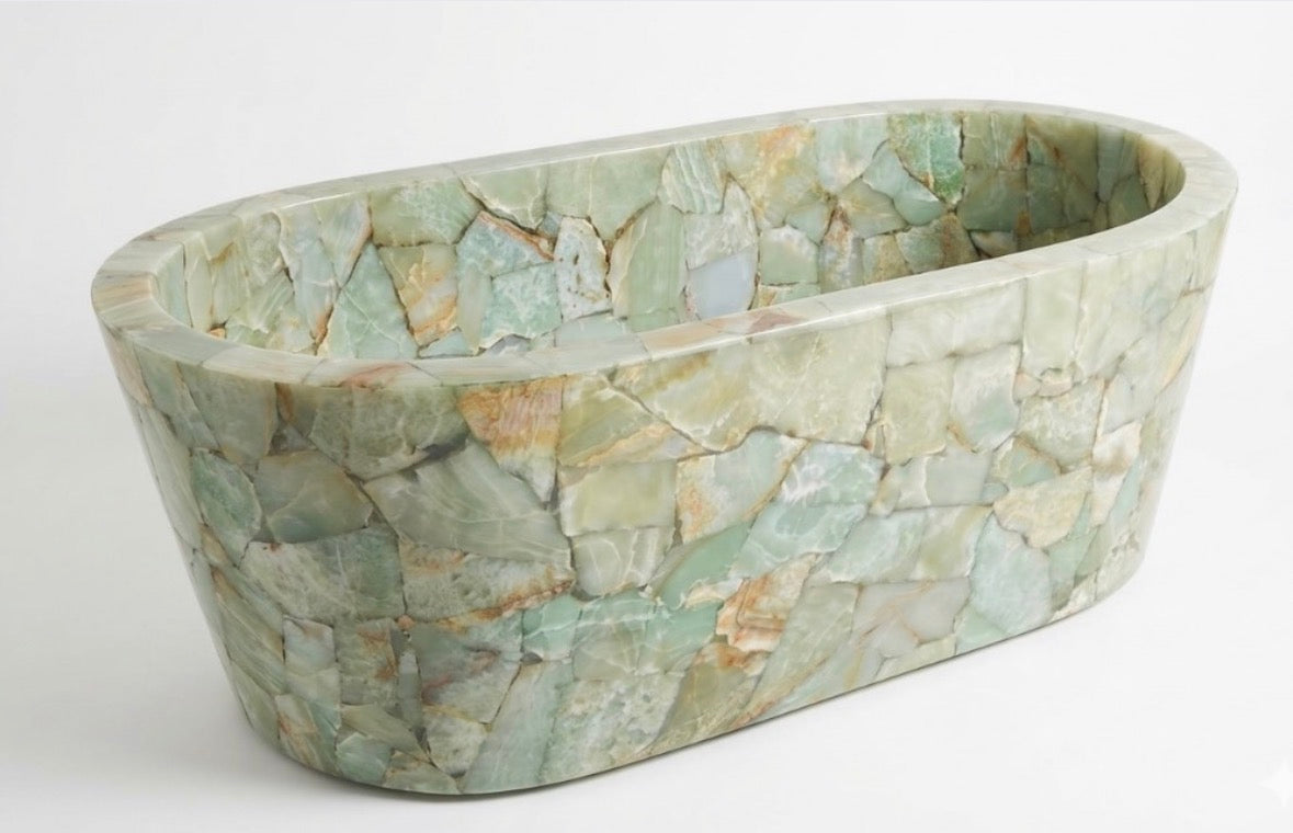 An oval, natural stone bath with a mosaic pattern of light green, beige, and gray polished fragments, designed by HC Homewares.