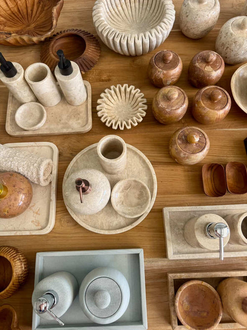A collection of artisanal soap dispensers, bathroom accessories, and bowls in natural stone and wood finishes crafted by HC Homewares.