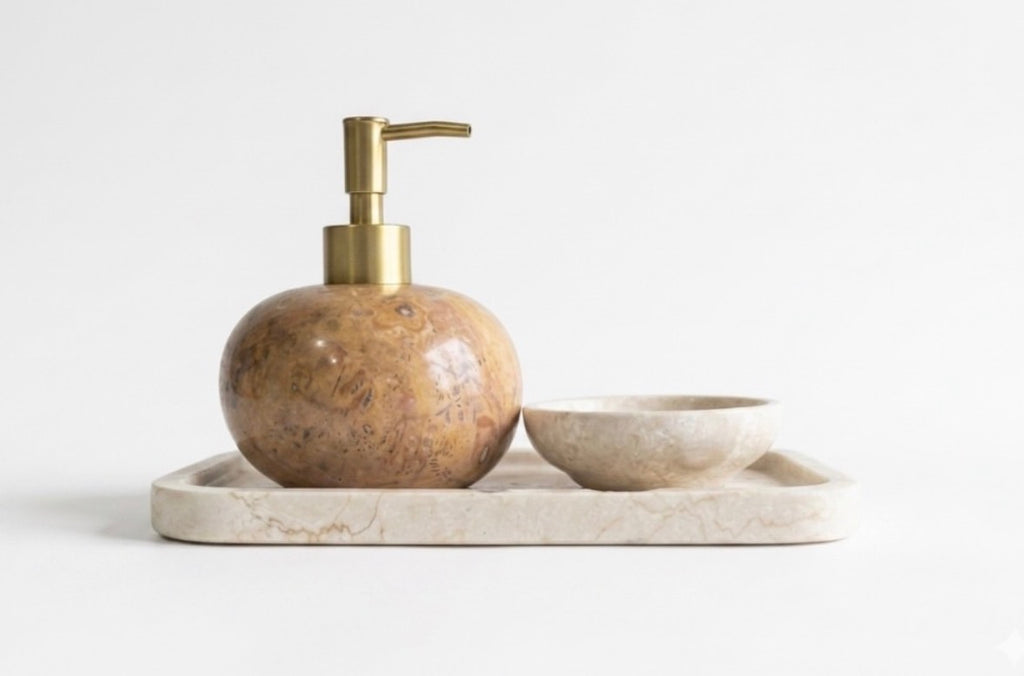 A bathroom accessory set featuring a round marble soap dispenser with a brass pump, a matching marble soap bowl, and a rectangular marble tray, designed to be mix-matched to suit your personal style.