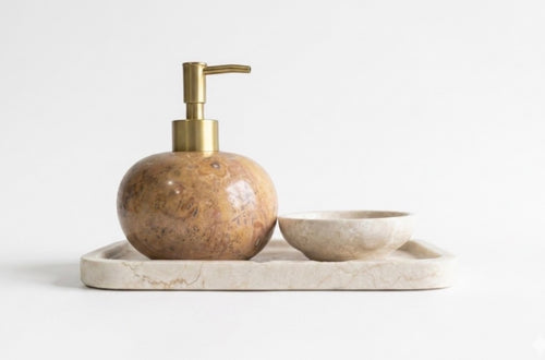 A bathroom accessory set featuring a round marble soap dispenser with a brass pump, a matching marble soap bowl, and a rectangular marble tray, designed to be mix-matched to suit your personal style.