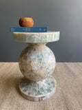 HC Homewares round marble side table with a mosaic green and beige stone pattern, styled with a blue book and a small wooden bowl on top.